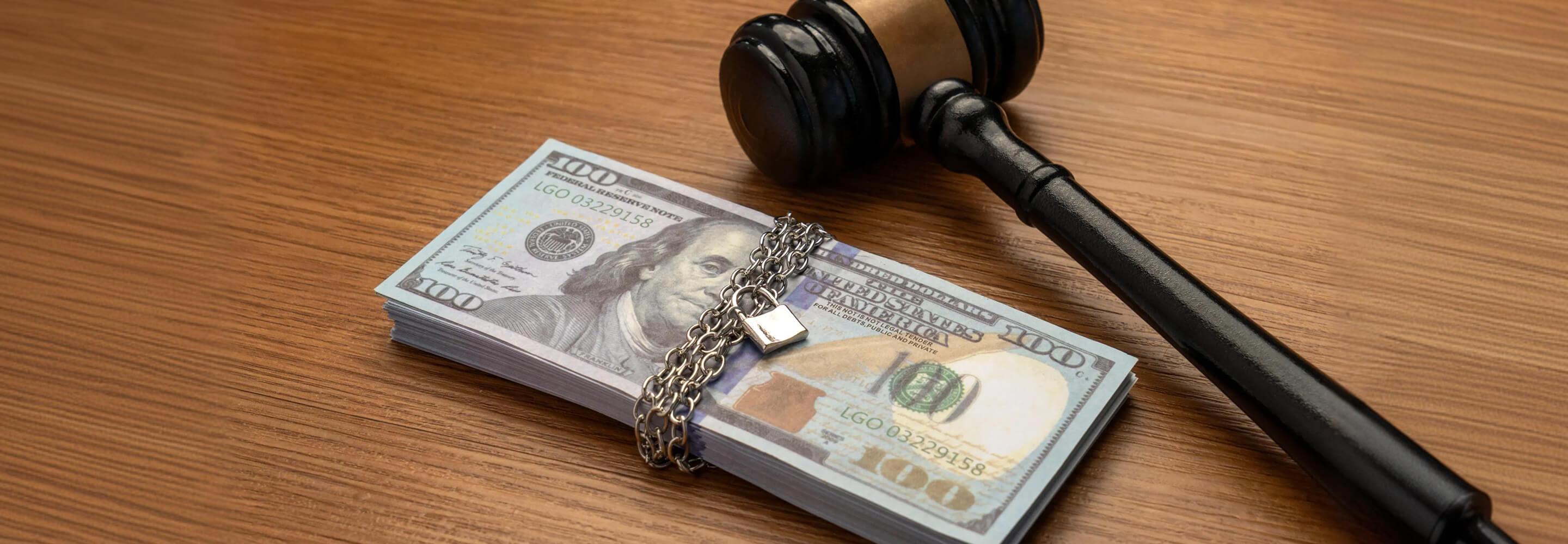 Stack of currency with a chain and padlock beside a judge’s gavel